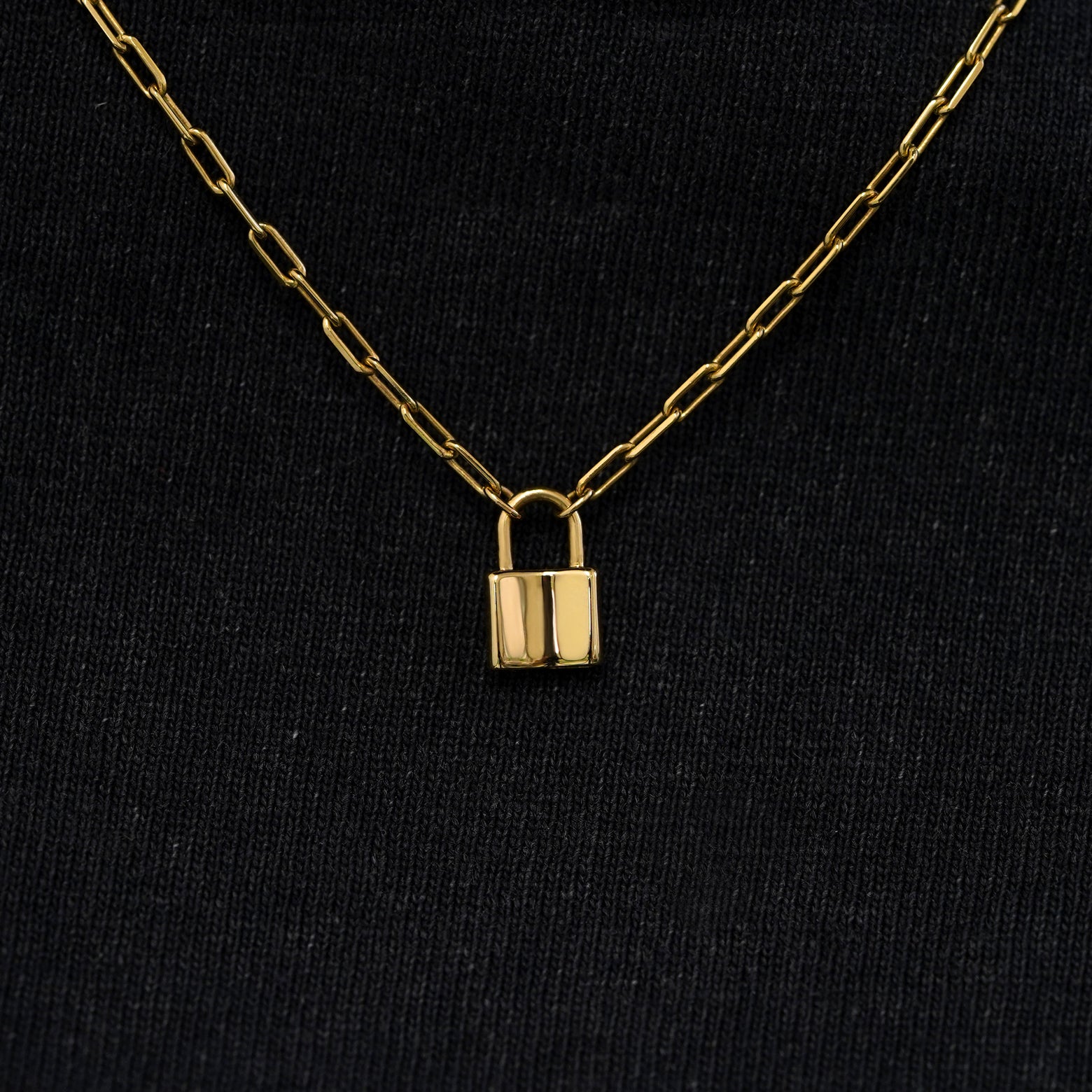 Close up view of a solid 14k yellow gold lock necklace against a model's black shirt