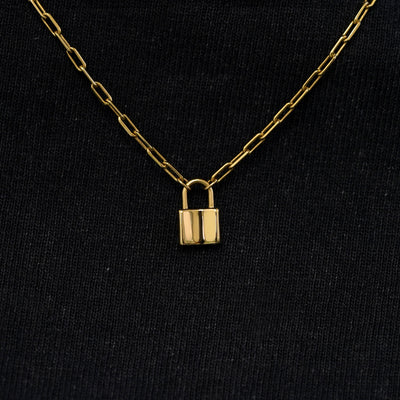 Close up view of a solid 14k yellow gold lock necklace against a model's black shirt