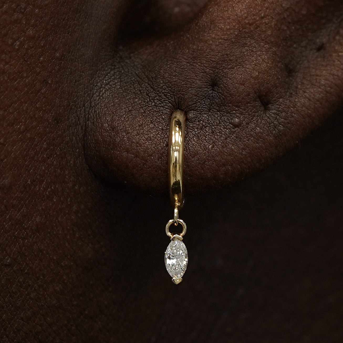 Close up view of a model's ear wearing a yellow gold Marquise Lab Diamond Dangle Huggie Hoop