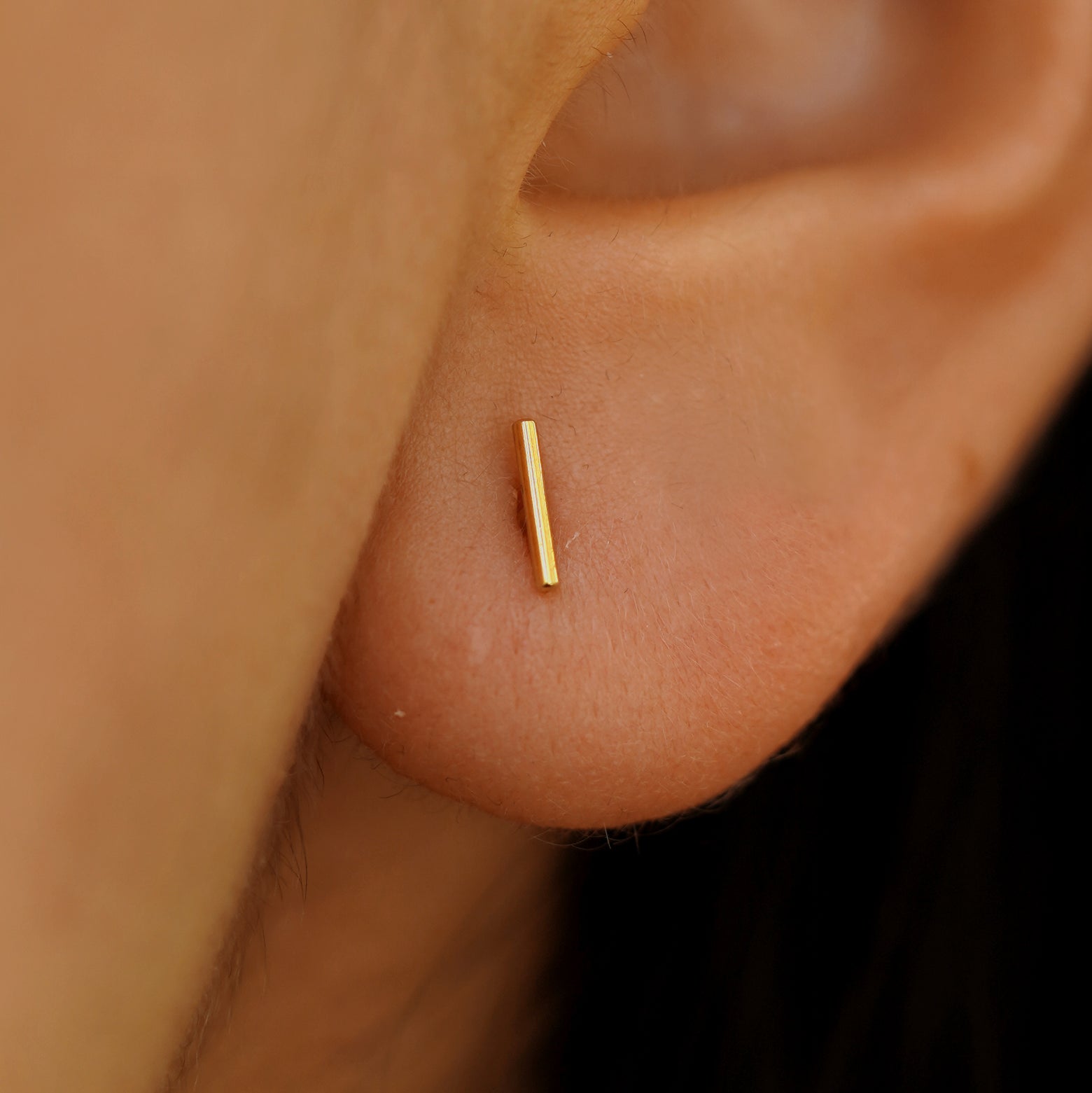 Close up of model's ear, they are wearing a yellow gold Medium Line Earring.