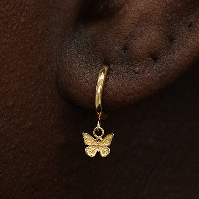 Close up view of a model's ear wearing a yellow gold Mini Butterfly Dangle Huggie Hoop