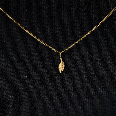 Close up view of a solid 14k yellow gold mini leaf necklace against a model's black shirt