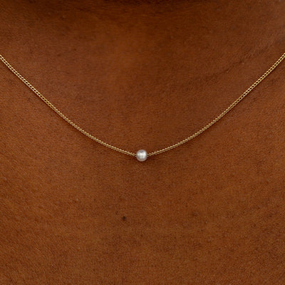 Close up view of a model's neck wearing a yellow gold Pearl Slide Necklace with a 2mm pearl