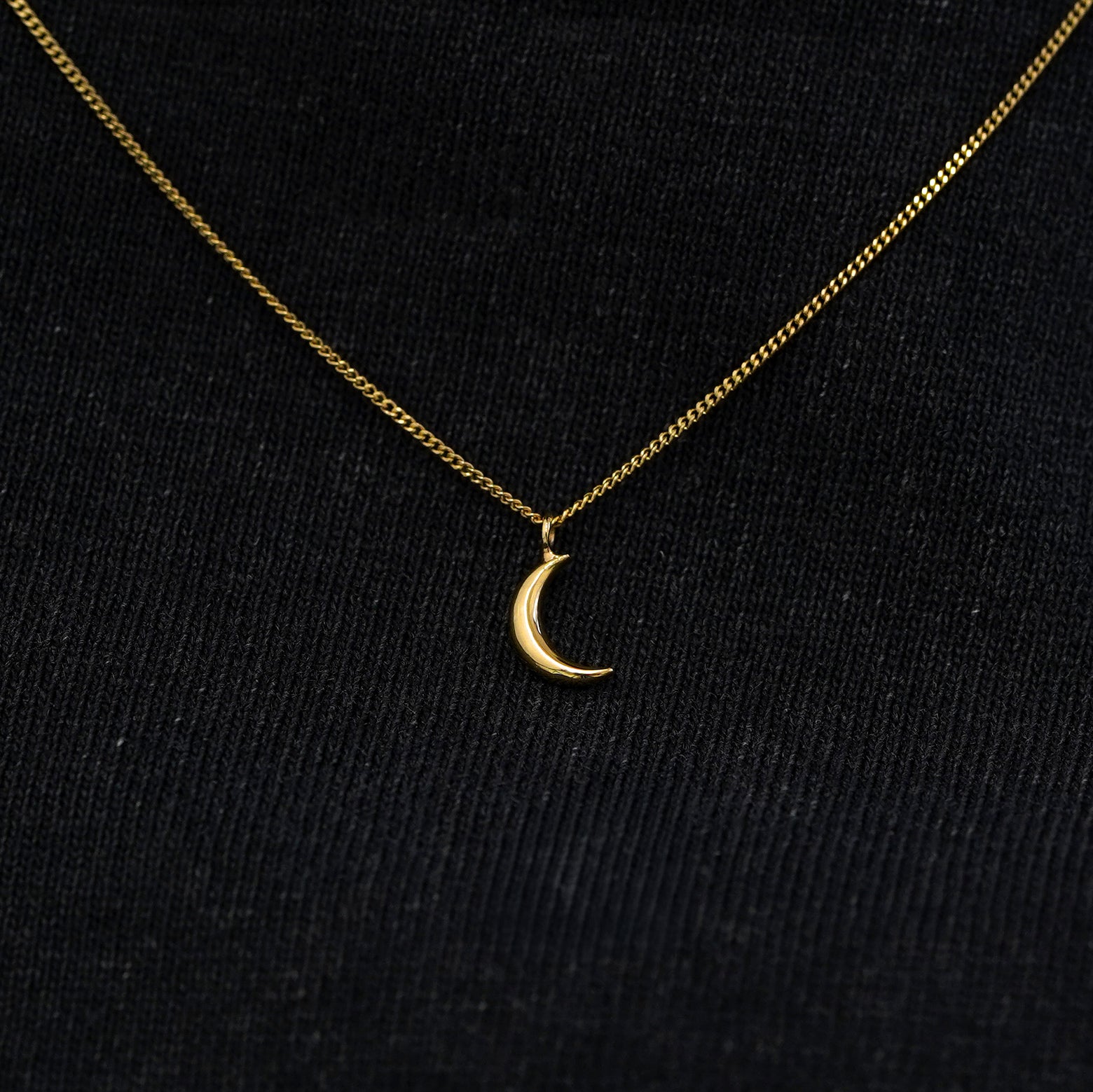 Close up view of a solid 14k yellow gold moon necklace against a model's black shirt
