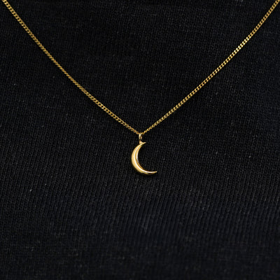 Close up view of a solid 14k yellow gold moon necklace against a model's black shirt