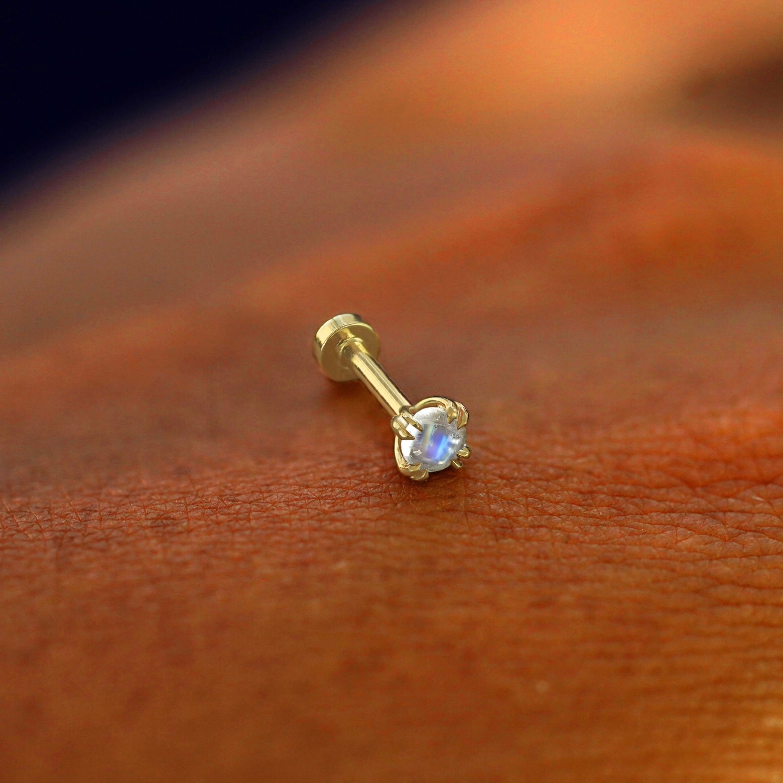 A solid 14k yellow gold Moonstone Flatback Piercing resting on the back of a model's hand