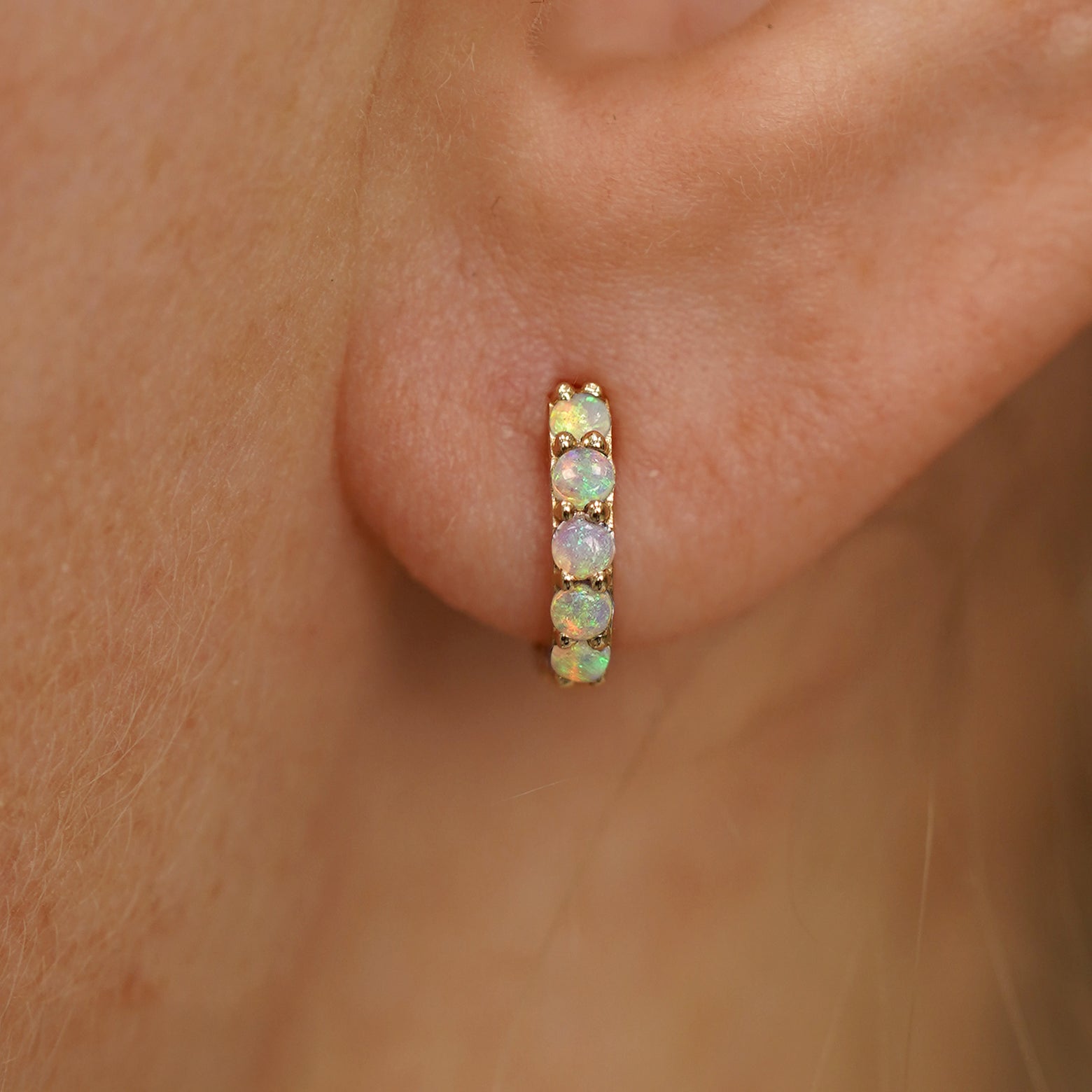 Close up view of a model's ear wearing a yellow gold Mini Opal Huggie Hoop