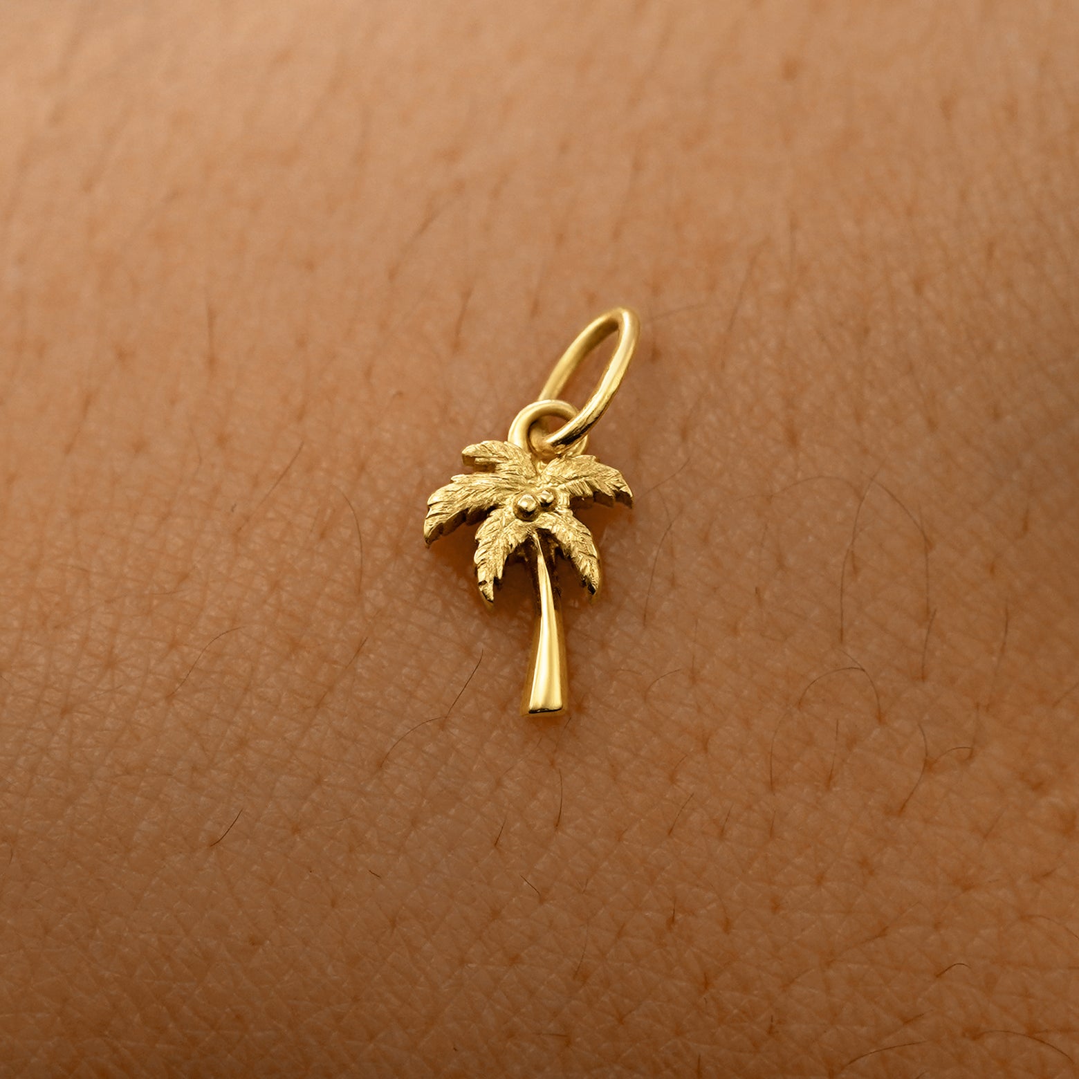 A solid 14k yellow gold Palm Tree Charm resting on the back of a model's hand