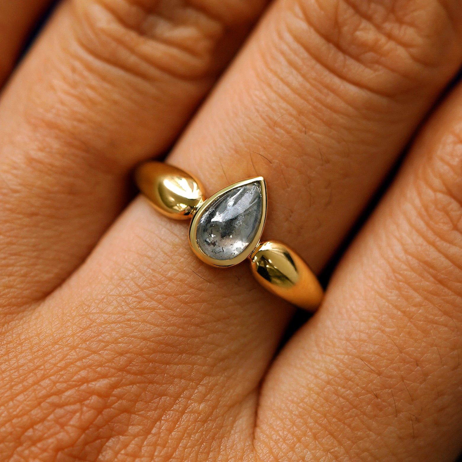 Close up view of a model's hand wearing a 14k yellow gold pear cabochon salt and pepper diamond engagement ring