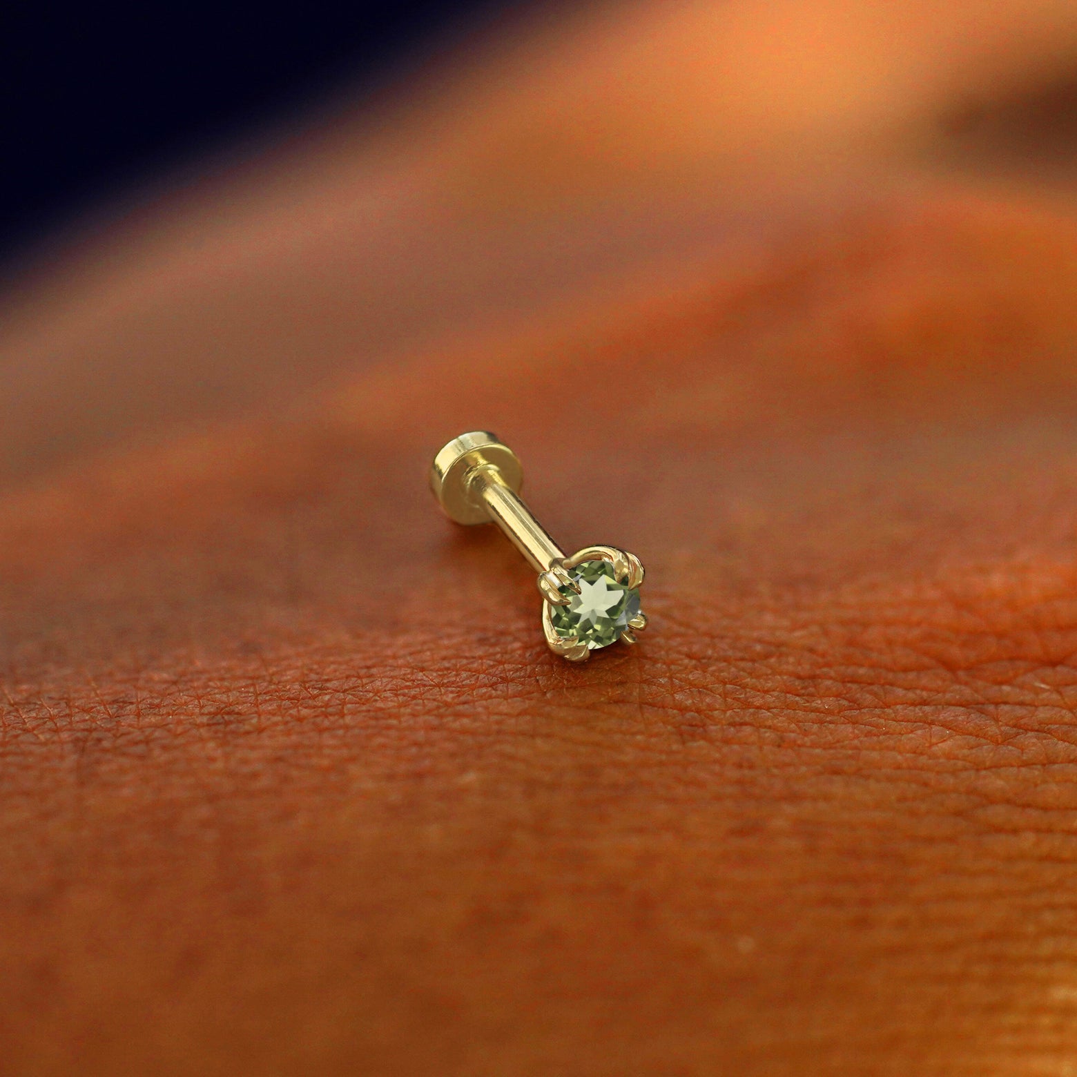 A solid 14k yellow gold Peridot Flatback Piercing resting on the back of a model's hand