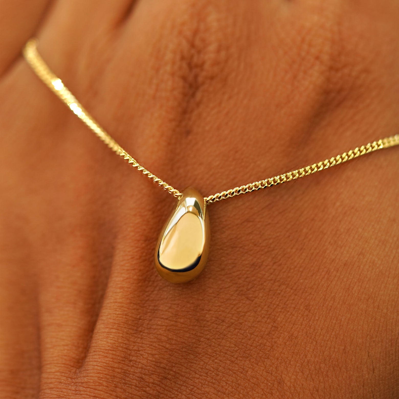 A model's holding a yellow gold Puffy Teardrop Necklace across the back of their hand