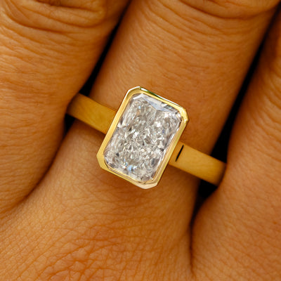 A solid 14k yellow gold Radiant Cut Lab Diamond Cathedral Ring on a model's finger