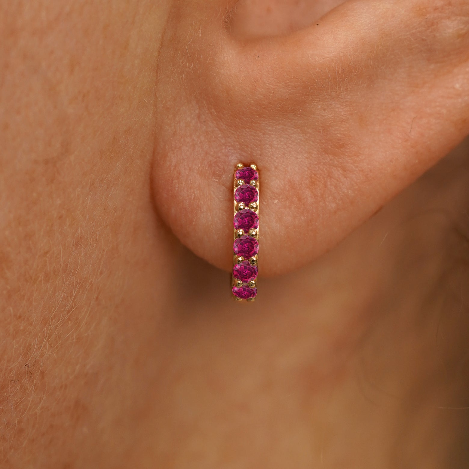 Close up view of a model's ear wearing a yellow gold Small Ruby Huggie Hoop