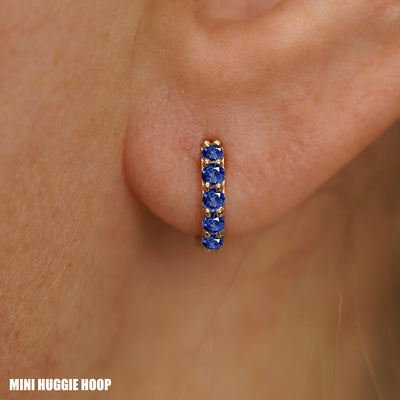 Close up view of a model's ear wearing a yellow gold Mini Blue Sapphire Huggie Hoop