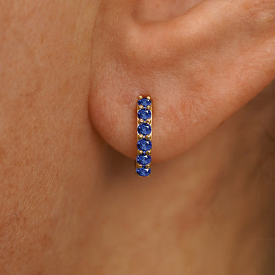 Close up view of a model's ear wearing a yellow gold Small Blue Sapphire Huggie Hoop