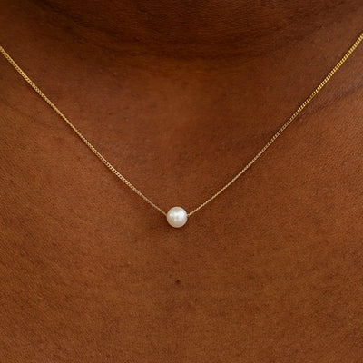 Close up view of a model's neck wearing a yellow gold Pearl Slide Necklace with a 4mm pearl