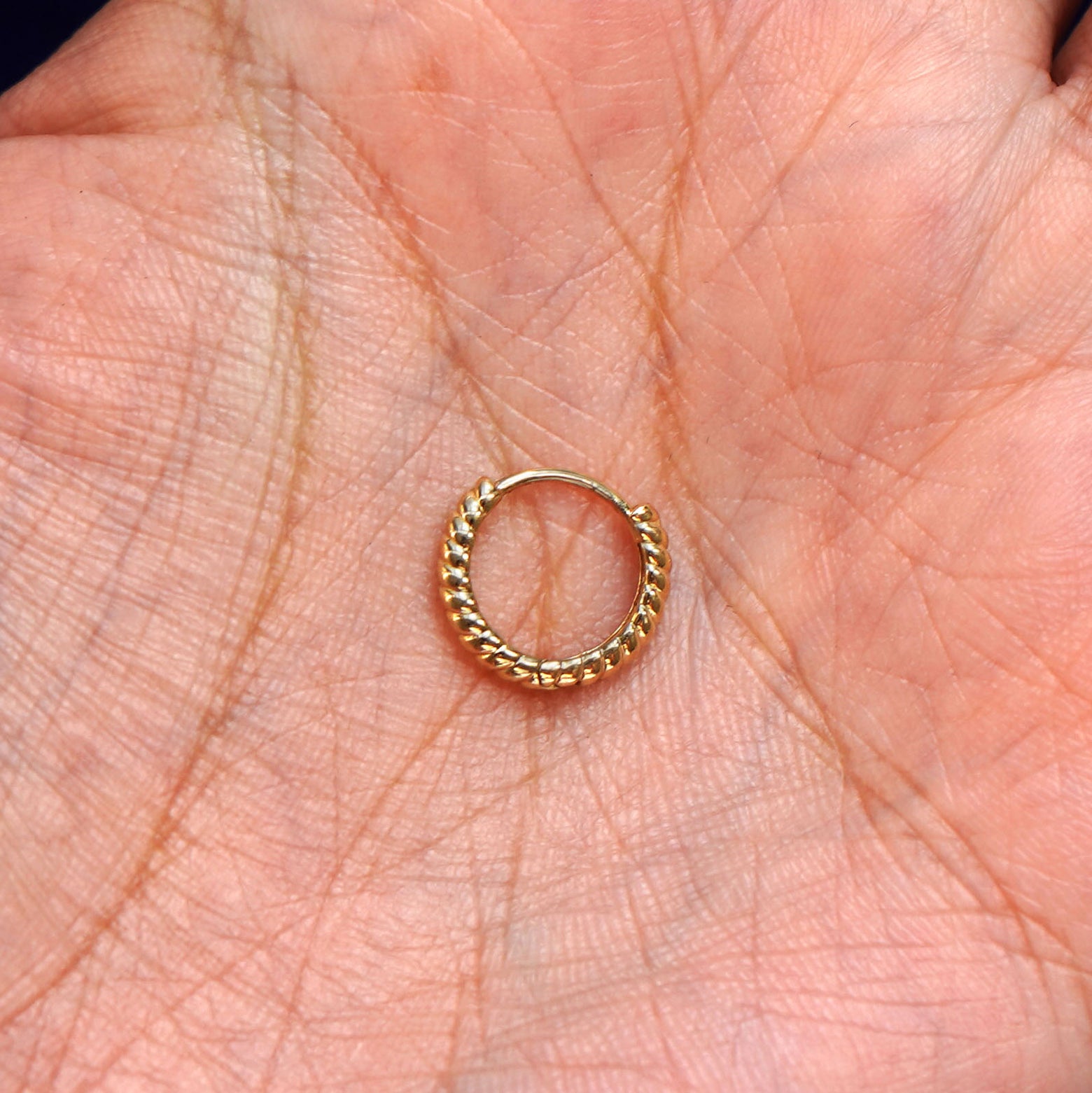A solid 14k yellow gold Small Rope Huggie Hoop Earring closed in a model's palm