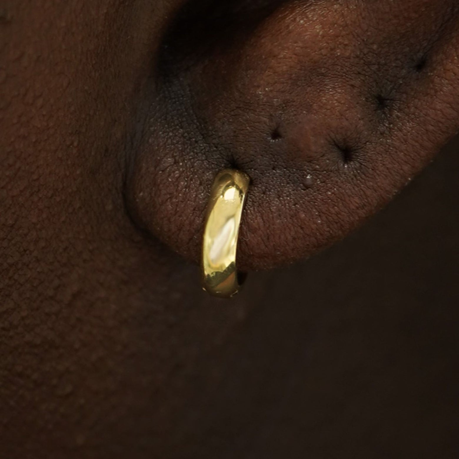 Close up view of a model's ear wearing a 14k gold Small Wide Huggie Hoop Earring