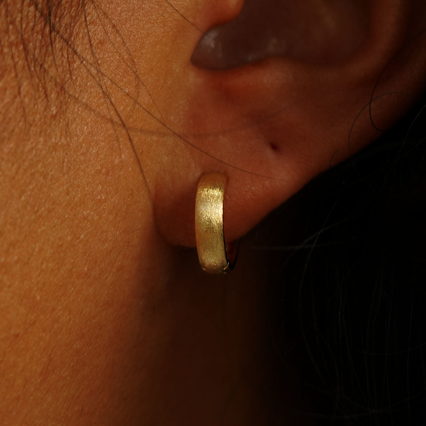 Close up view of a model's ear wearing a 14k gold Stardust Small Wide Huggie Hoops
