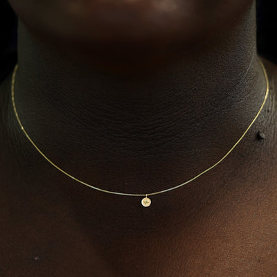 A solid yellow gold engraved star disk necklace on models neck