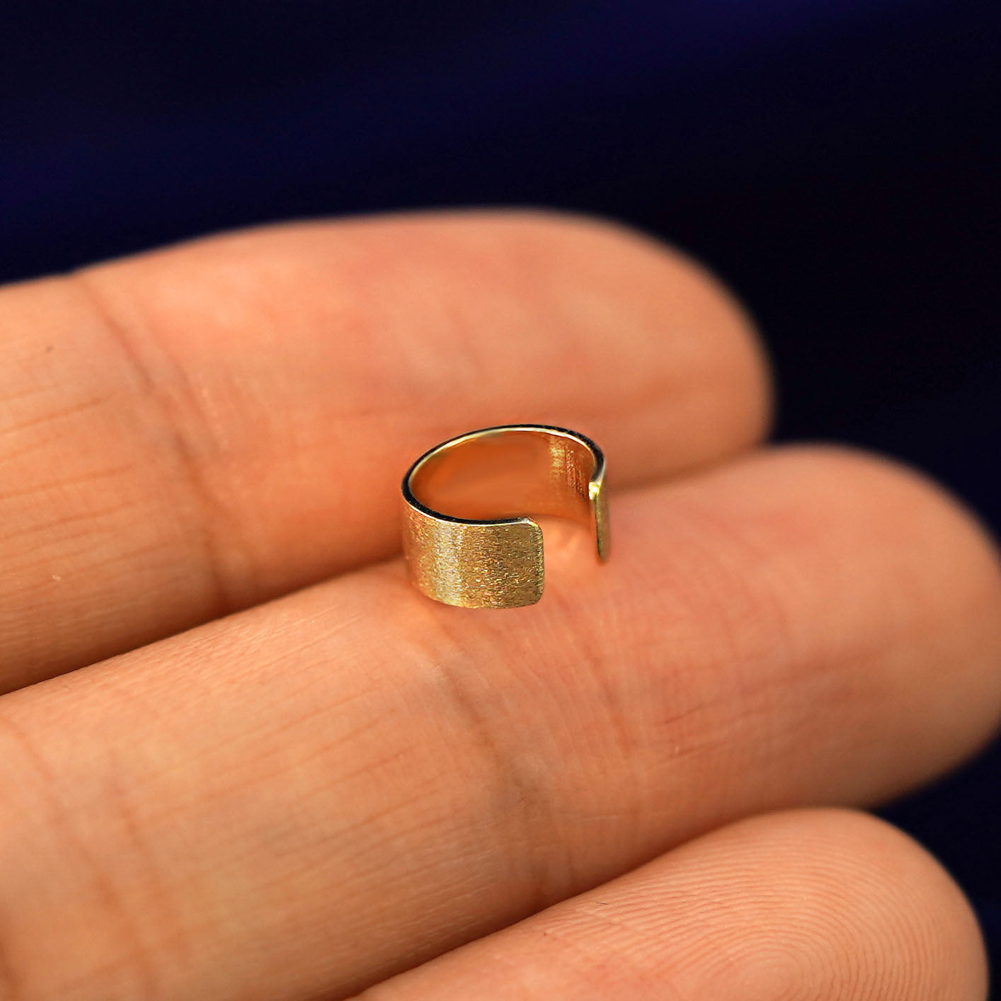 A solid yellow gold Thick Stardust Cuff earring resting on a model's fingertips