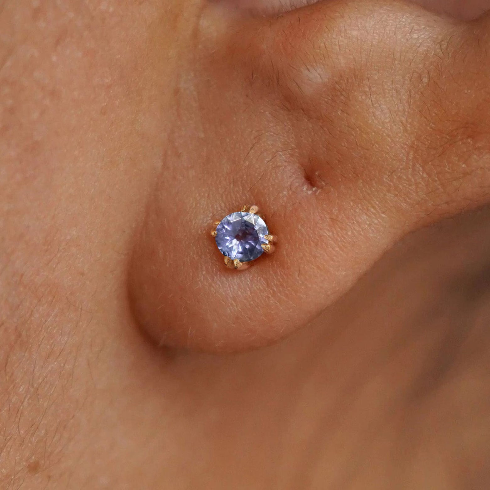 Close up view of a model's ear wearing a 14k yellow gold Tanzanite Earring