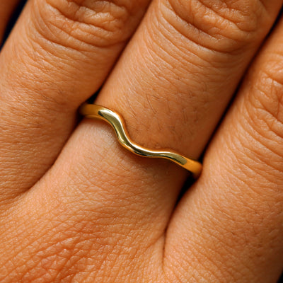 Close up view of a model's hand wearing a 14k yellow gold thin liquid band