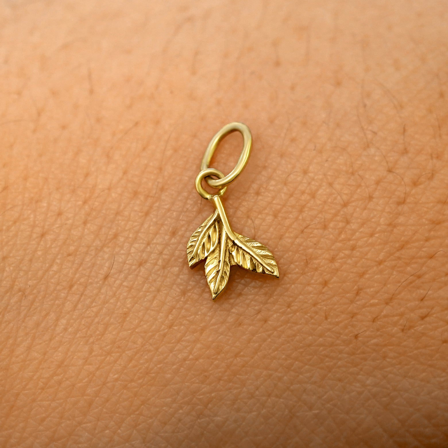 A solid 14k yellow gold 3 Leaves Charm resting on the back of a model's hand