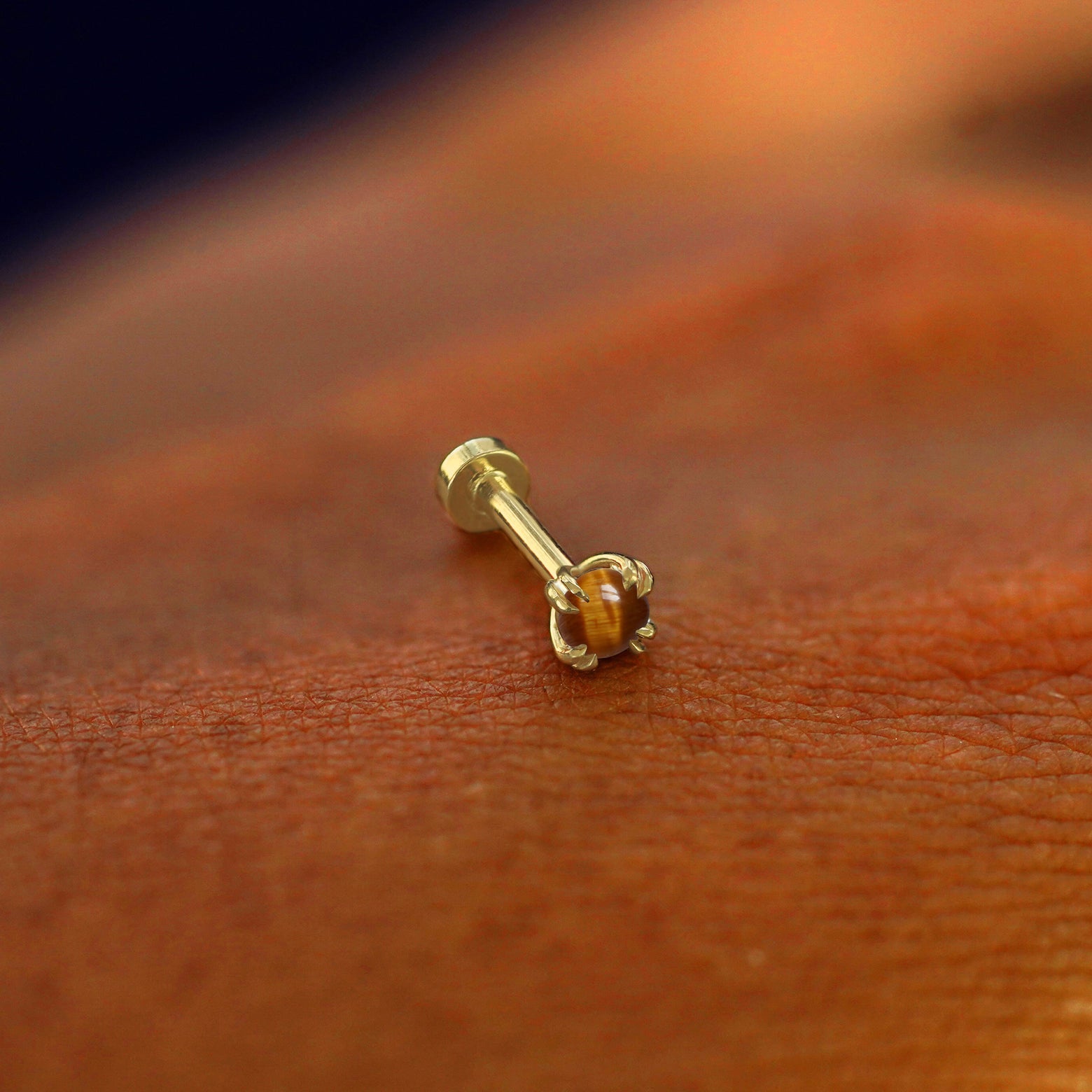 A solid 14k yellow gold Tiger Eye Flatback Piercing resting on the back of a model's hand