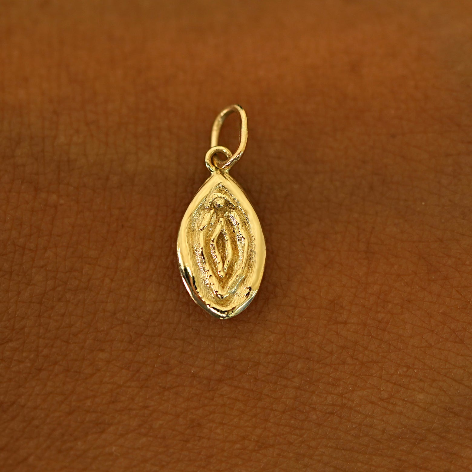 A solid 14k yellow gold Vulva Charm resting on the back of a model's hand