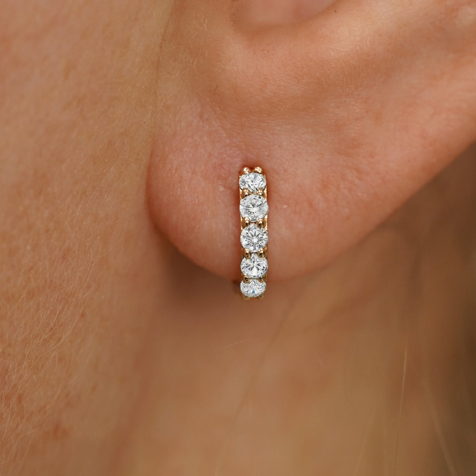Close up view of a model's ear wearing a yellow gold Mini Lab White Diamond Huggie Hoop