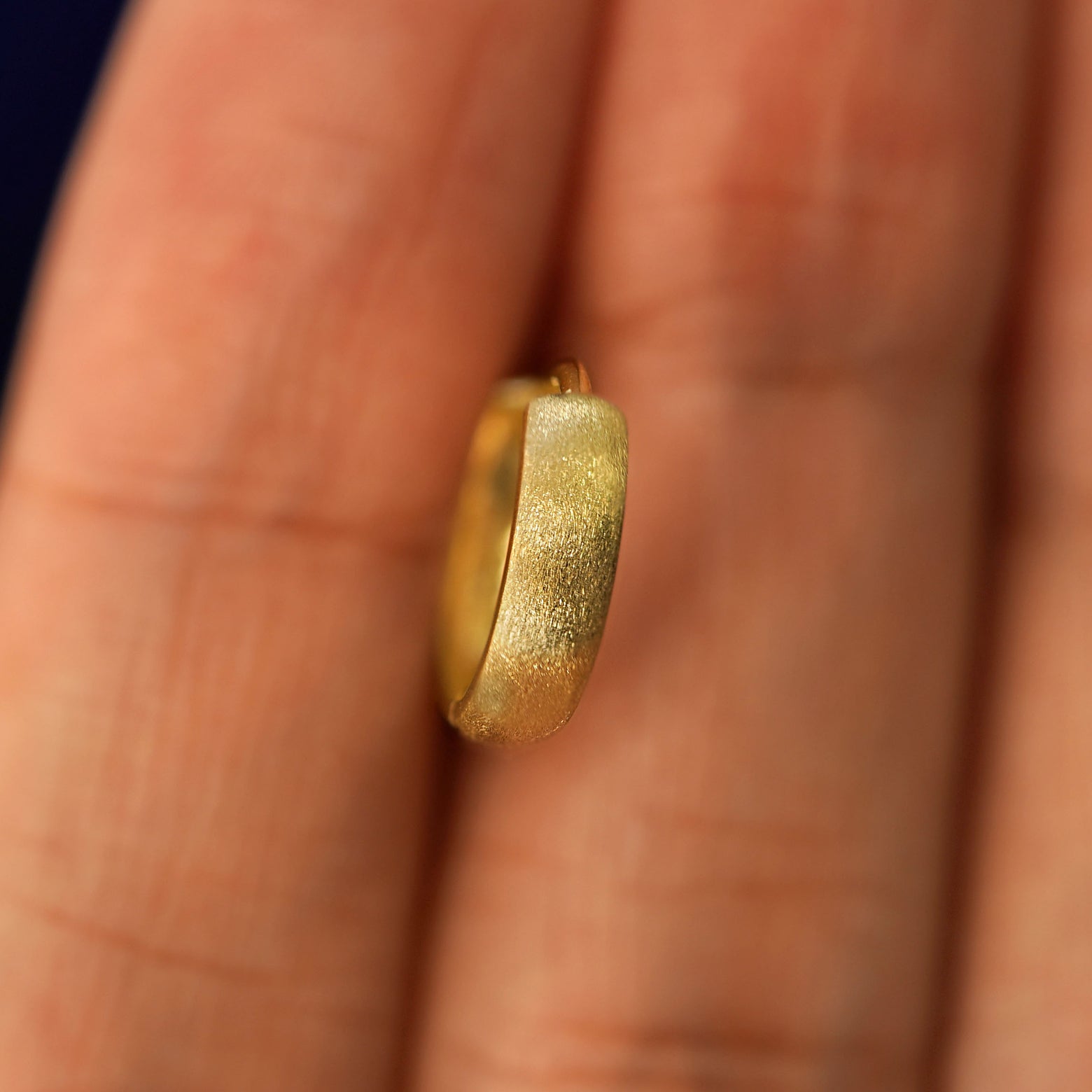 A yellow gold Stardust Small Thick Huggie Hoop Earring held in between a model's fingers to show the hoops thickness