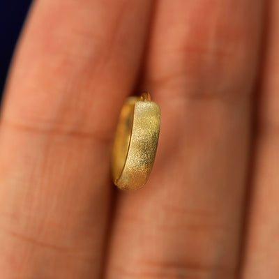A yellow gold Stardust Small Thick Huggie Hoop Earring held in between a model's fingers to show the hoops thickness