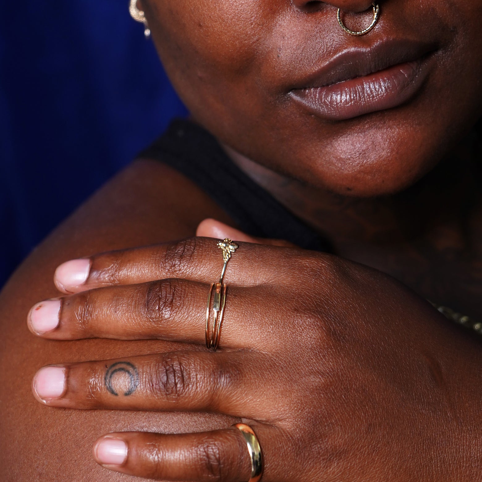 A model with their hand on their shoulder wearing a Bar Ring between two Line Rings, a Bee Ring, and a Curvy Mirror Band