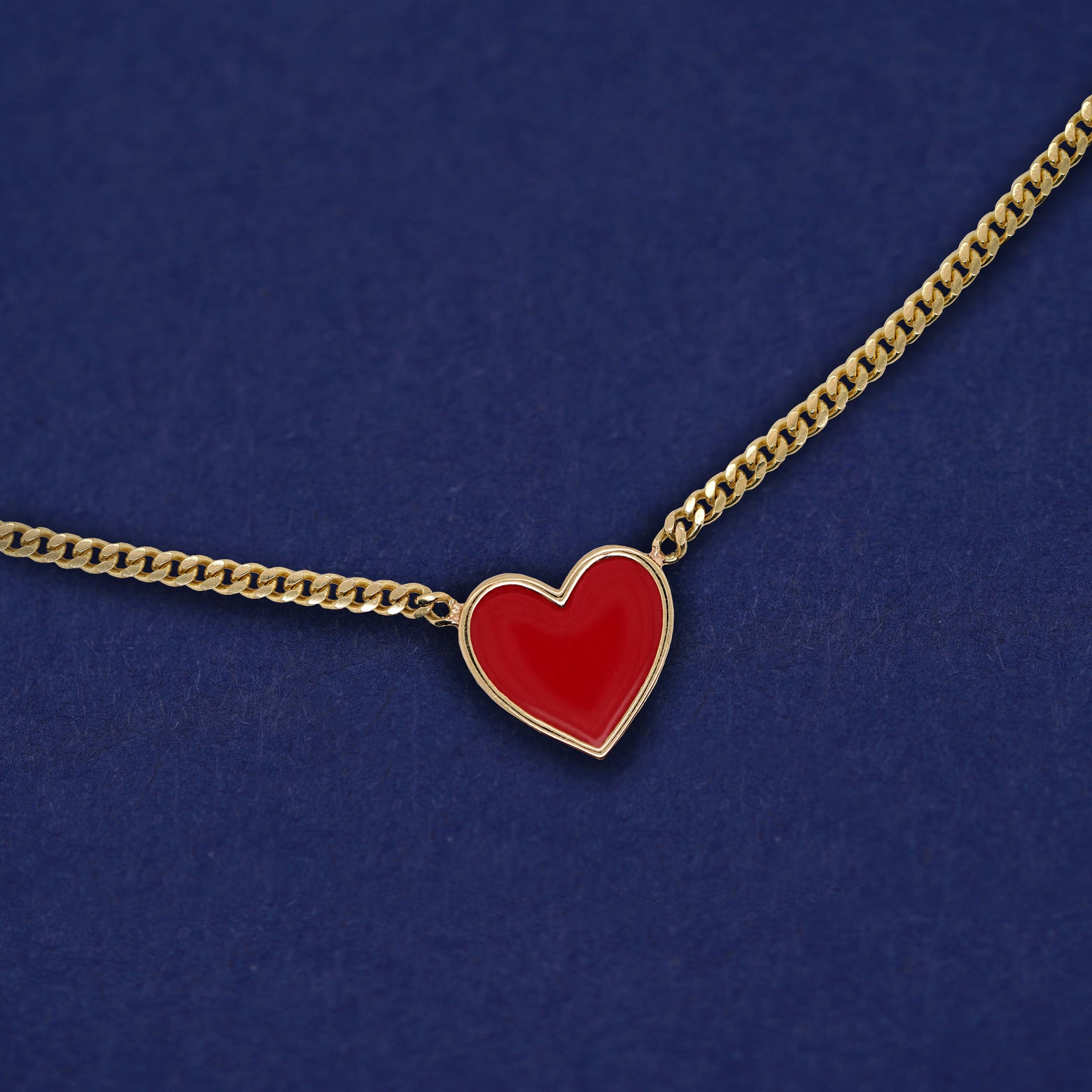 A solid 14k gold red enamel heart necklace on a dark blue background