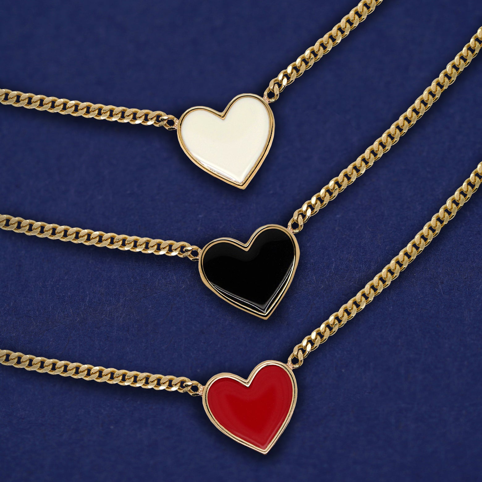 Three solid gold enamel heart necklaces shown in options of white, black, and red enamel
