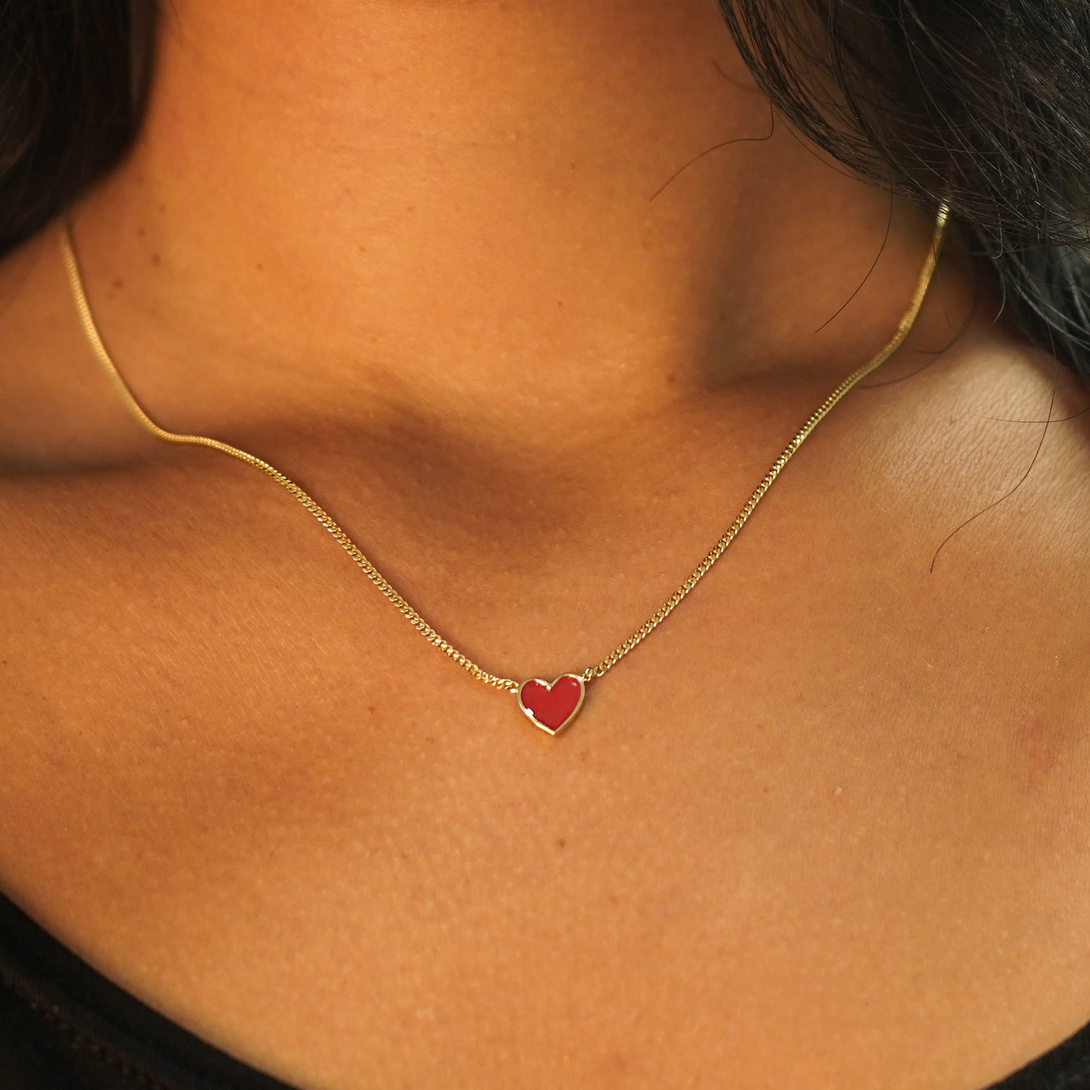 A model's neck wearing a yellow gold red enamel heart necklace