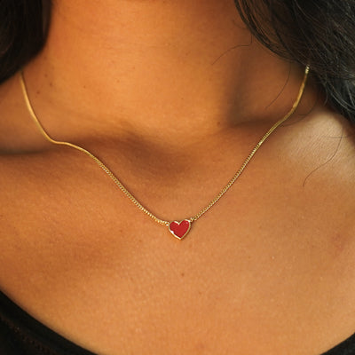 A model's neck wearing a yellow gold red enamel heart necklace