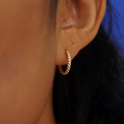Close up view of a model's ear wearing a yellow gold Small Rope Huggie Hoop