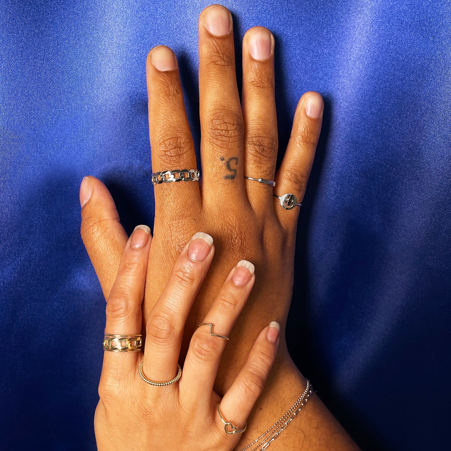 A model wearing yellow gold rings touching the wrist of a model wearing white gold rings