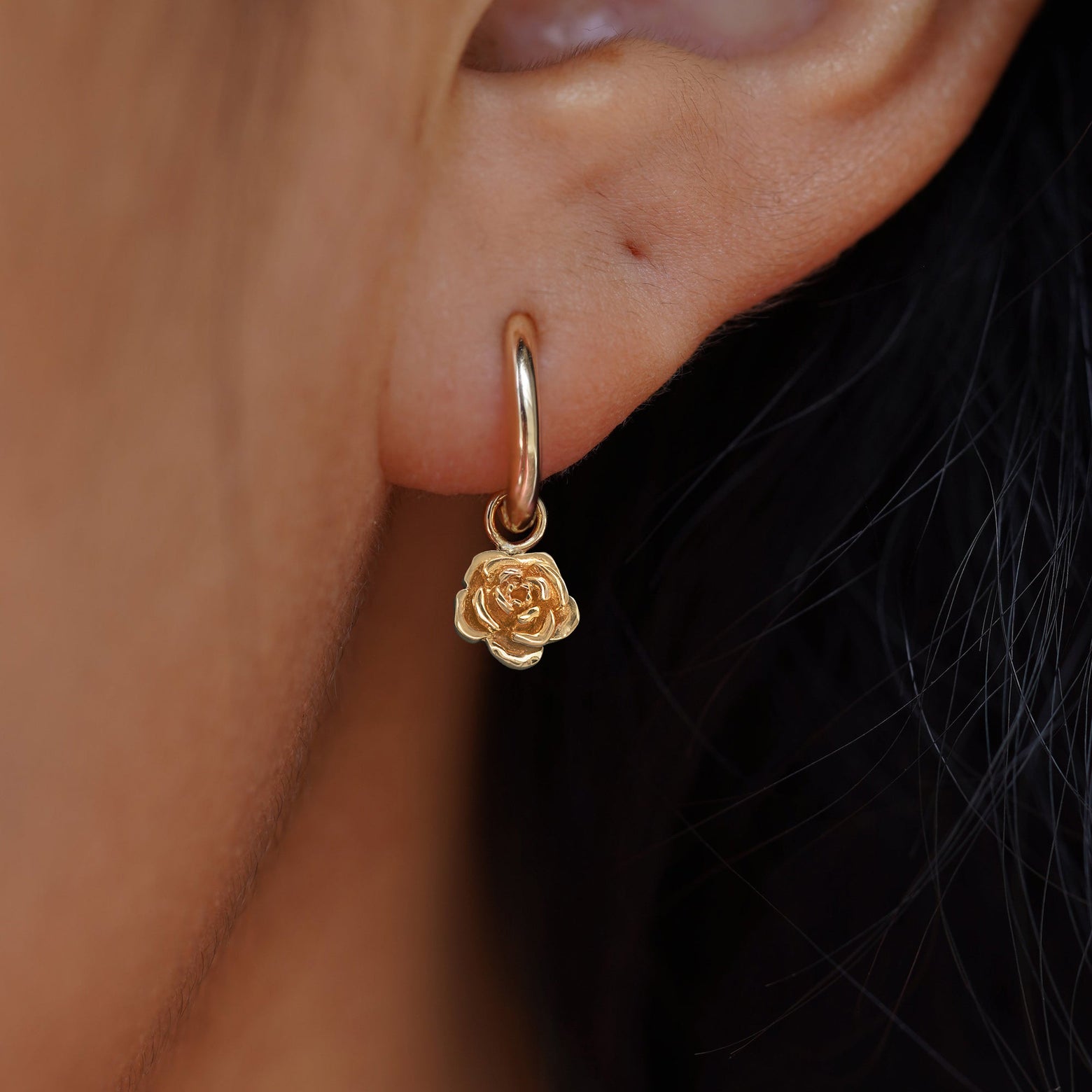 Close up view of a model's ear wearing a yellow gold Rose Charm on a Small Curvy Huggie Hoop